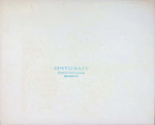 Zintgraff photographer mark (blank verso) — Essentially blank cream card back of a photograph, bearing only a faint blue printed studio stamp: "ZINTGRAFF / PHOTOGRAPHER / SAN ANTONIO[?]".