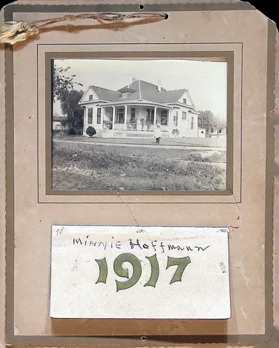 Minnie Hoffmann house, 1917 — 1917 — Photograph of a two-story house with a wraparound porch, mounted on a tasseled card. A caption card below reads "Minnie Hoffmann" with a decorative "1917".