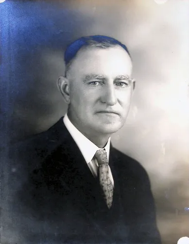 Portrait of an older man — Black-and-white studio portrait of an older man with graying hair, wearing a dark suit and patterned tie. No text visible on the front.