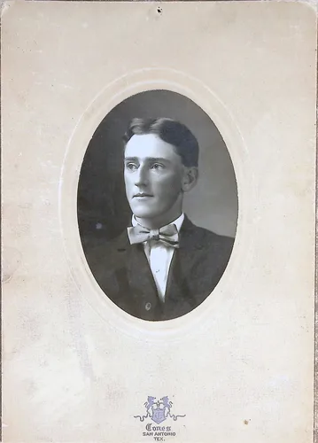 Portrait of a young man — Oval-vignette studio portrait of a young man with a bow tie and dark coat, mounted on a card with a crest and studio imprint reading "Corn[?]ss[?] San Antonio, Tex.". No name visible.