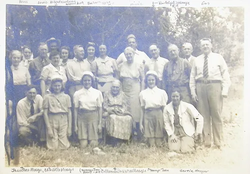 Menger family group portrait — Outdoor group portrait of about sixteen people in three rows in front of trees. Handwritten names along the edges include (top) "Helen", "Louis", "Alfred Kaufeldt[?]", "Barbara[?]", "Rudolph Menger[?]", "Gus"; (bottom) "Theodore Menger", "Estelle Menger", "Catherine[?]", "Barbara Menger[?]", "Menger Twin", "Gertie Menger[?]". Several names are faint and uncertain.