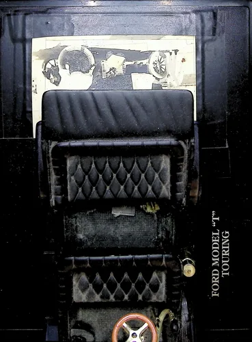 Ford Model T Touring (interior) — Color close-up photo of a dark model car's tufted seats and interior, captioned vertically "FORD MODEL \"T\" TOURING". An old black-and-white photo is tucked behind the seat at top.